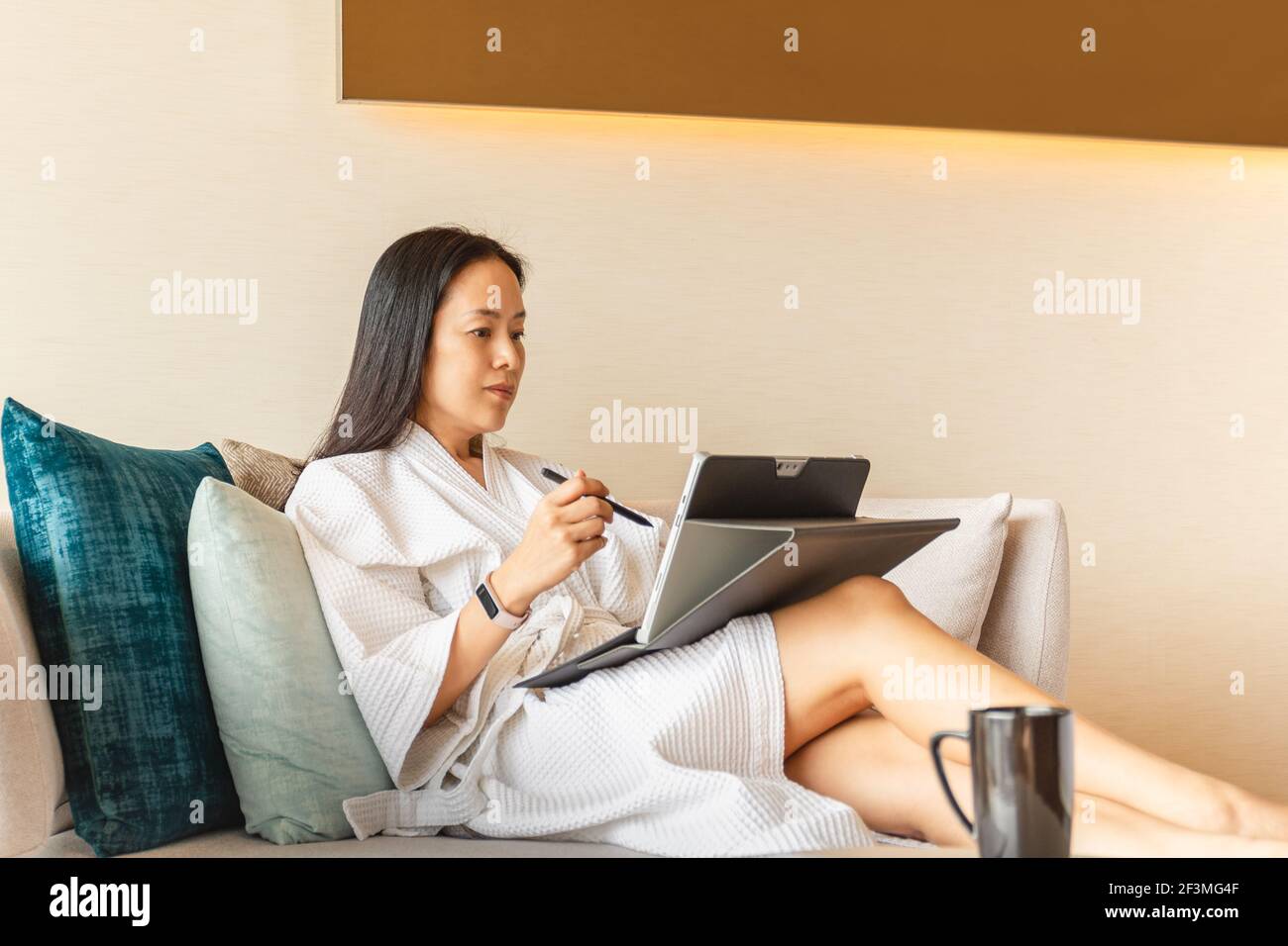 Woman in dressing gown sit on couch in hotel room working on laptop ...