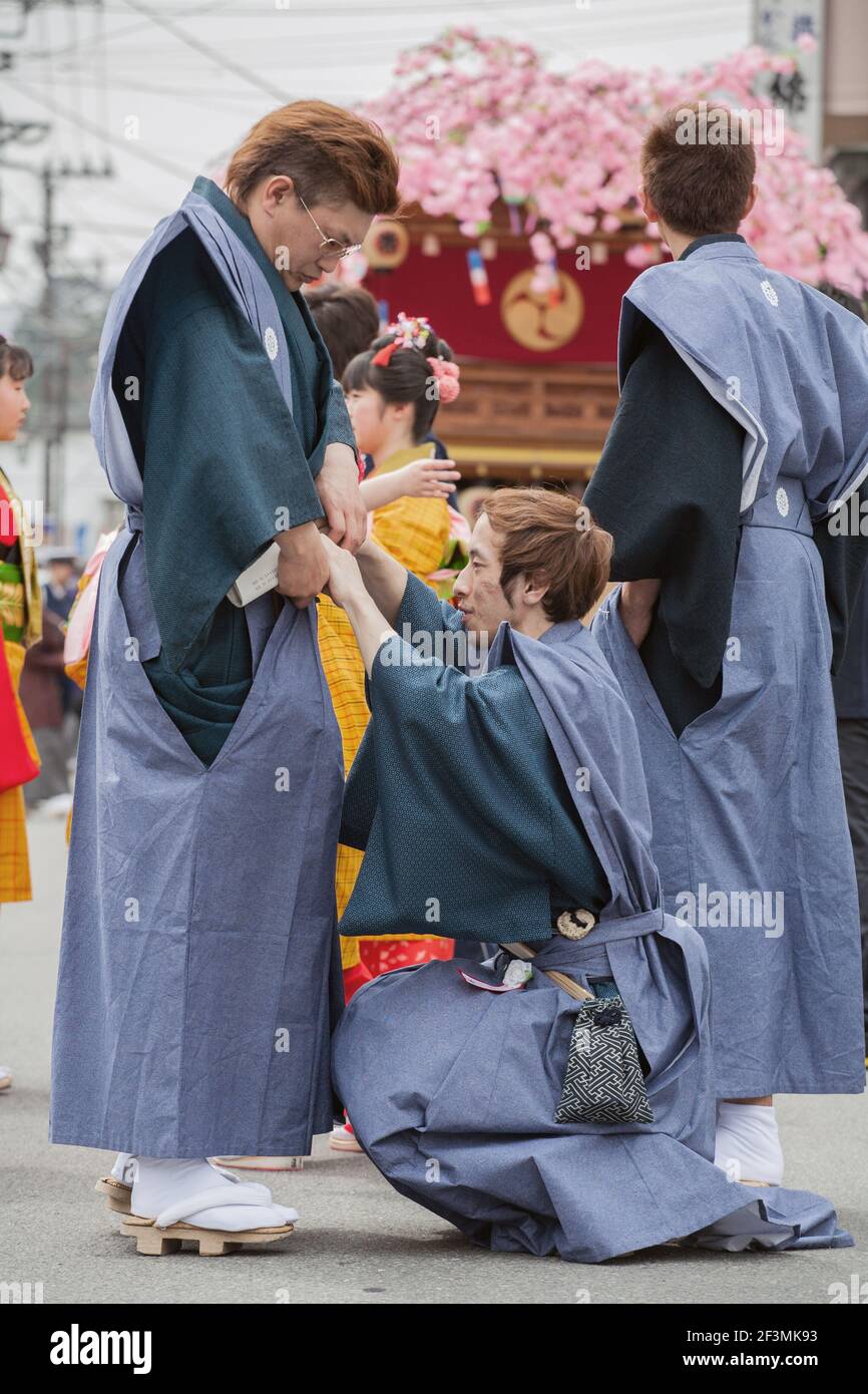 Japanese male crouches to adjust another male participant's kimono at the annual Yayoi Matsuri to celebrate the start of spring, Nikko, Japan Stock Photo