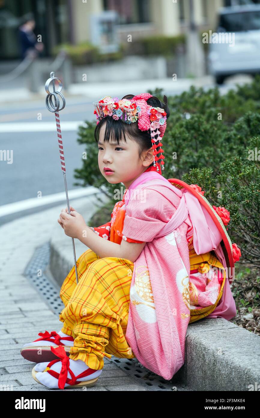 Young Japanese female clutching ceremonial staff sits on kerb waiting