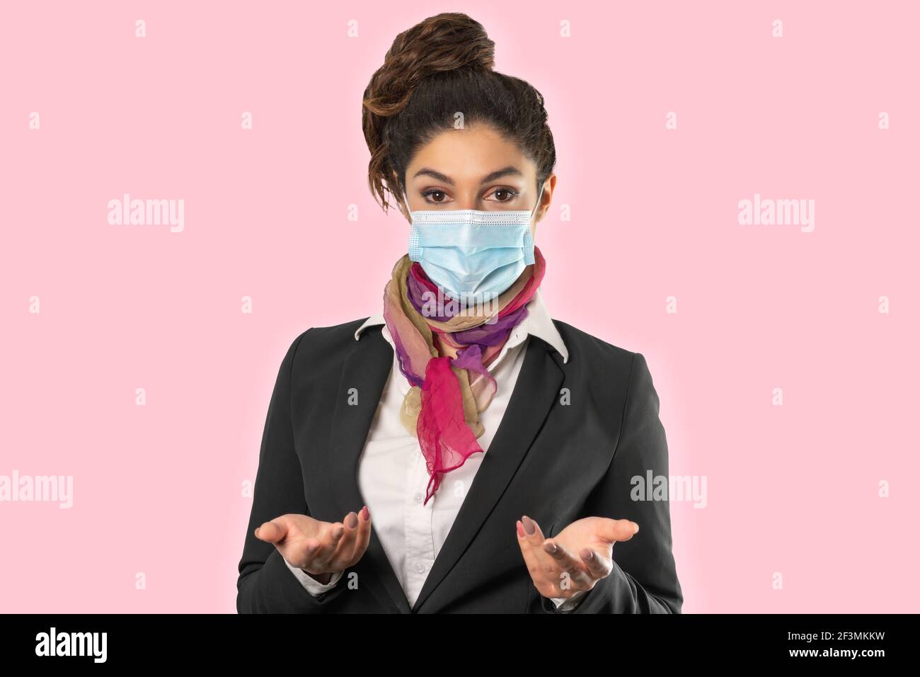 A beautiful flight attendant with surgical mask, multicolored scarf and black jacket. Subject on a pink background. Perfect shot for women at work, pa Stock Photo
