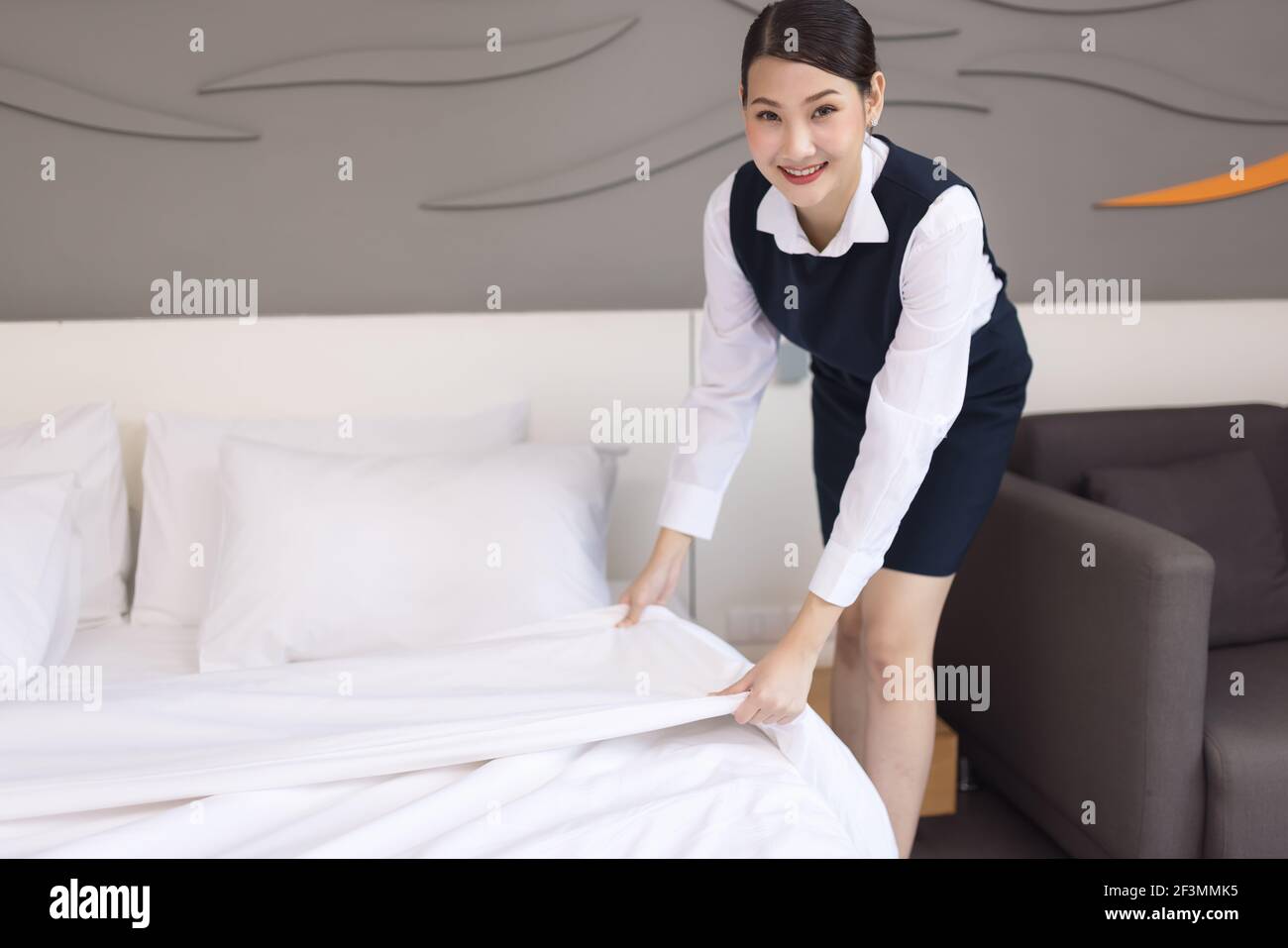 Asia maid making bed in hotel room, setting up pillow on bed Stock