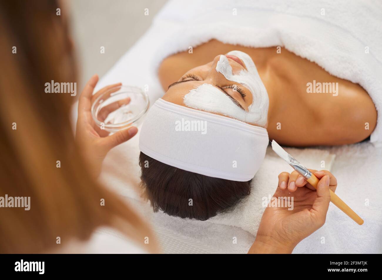 Beautician covering woman facial skin with moisturizing mask during skincare procedure Stock Photo