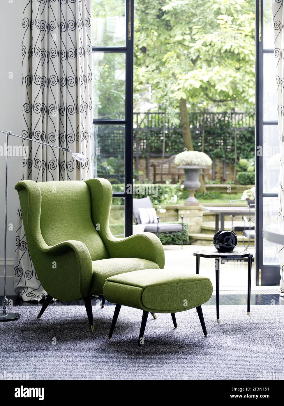 Green armchair and footstool in front of French doors with view to