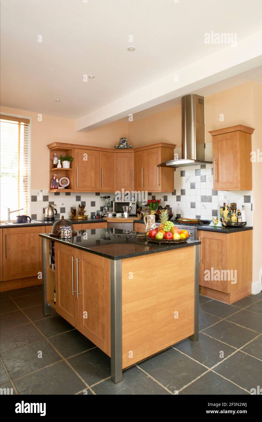 Modern kitchen with stone tiled floor, wood units, cooker extractor hood and central kitchen island Stock Photo