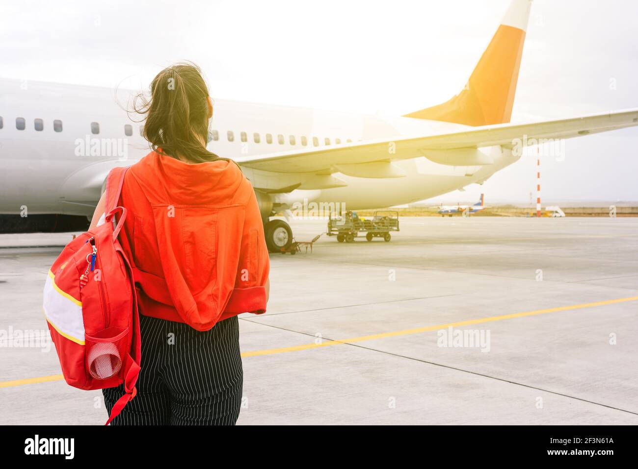 The girl is standing near the plane waiting for departure. Boarding passengers on the flight. Young traveler at the airport. Travel and tourism concep Stock Photo