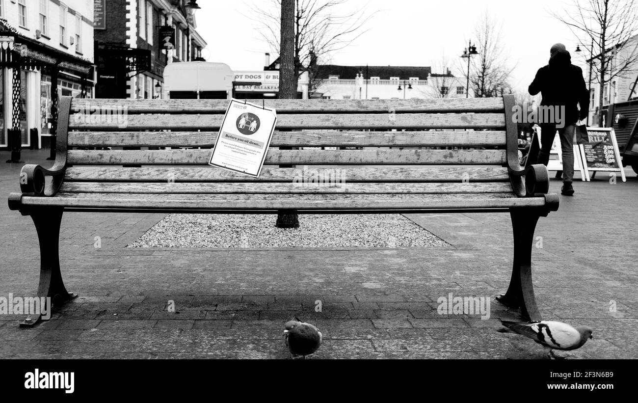 London UK, March 17 2021, Empty Wooden Seat With No People And A Warning Sign for Social Distancing Stock Photo