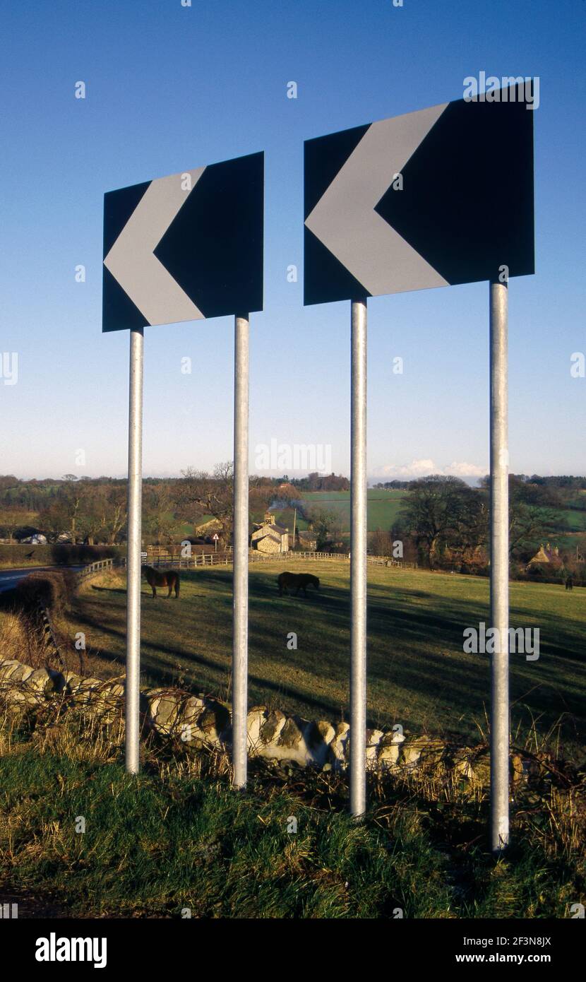 Bedlam. Near Ripley. Chevrons, road signs. Slow down, bend. Tall posts. Stock Photo