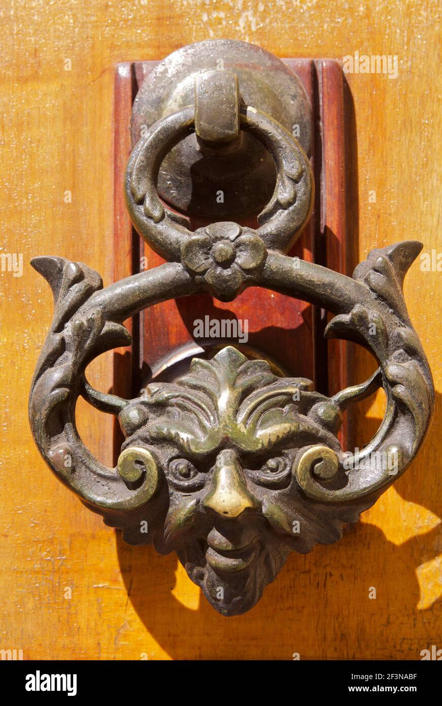 An ornate door knocker in the shape of a human face, with a wicked 