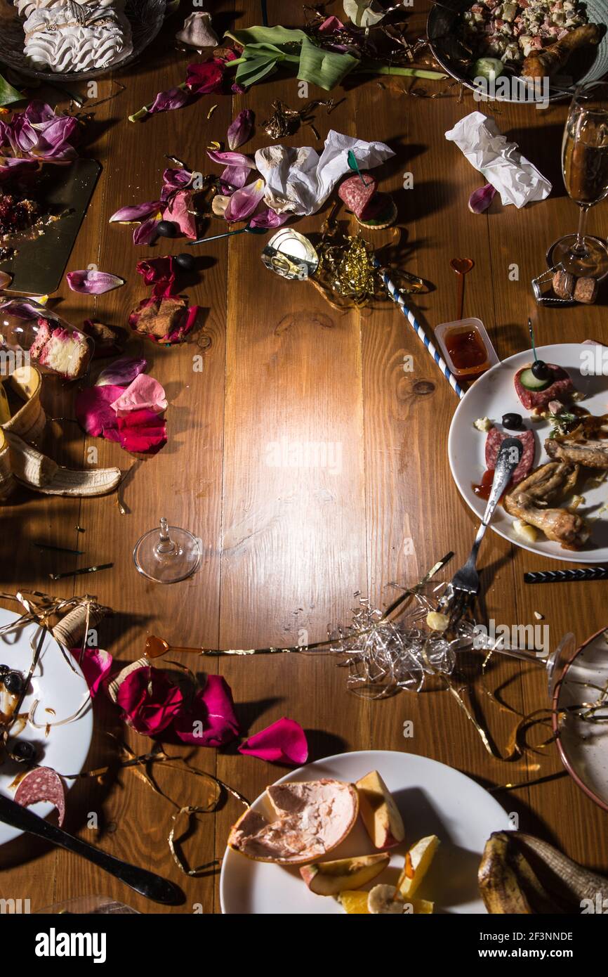 Early morning after the party. Glasses and plates on the table with confetti and serpentine, leftovers, flower petals Stock Photo