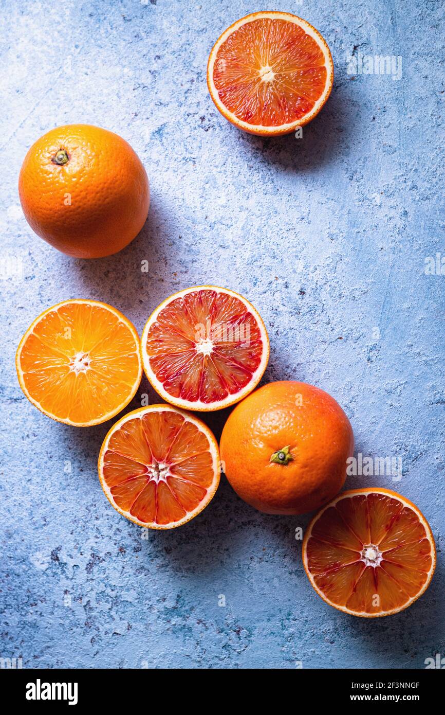 Sliced and whole ripe juicy blood oranges on blue table. Stock Photo