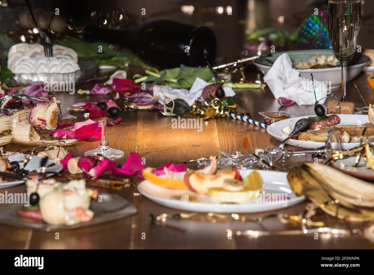 Early morning after the party. Glasses and plates on the table with confetti and serpentine, leftovers, flower petals Stock Photo