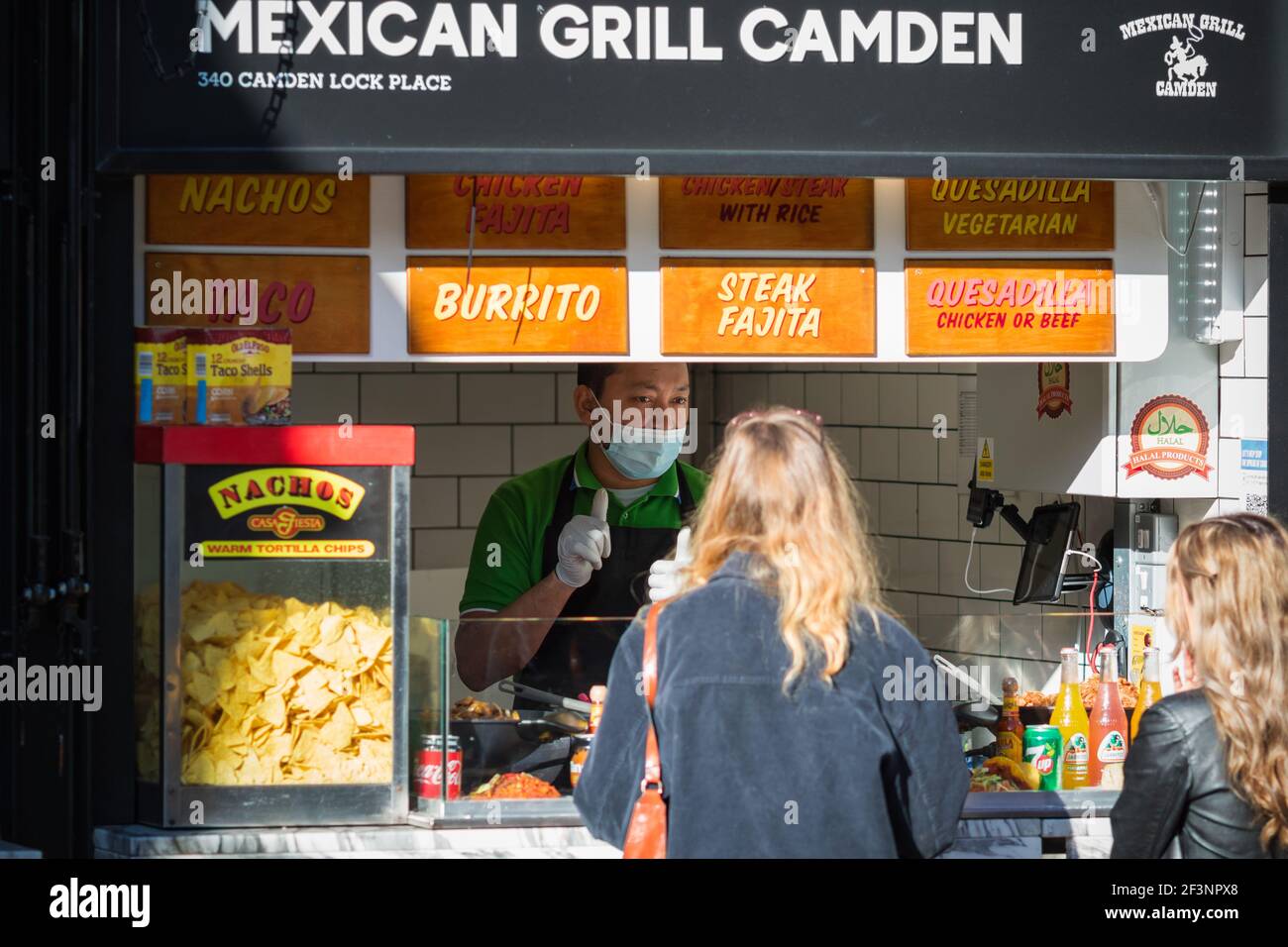 London, UK - 26 February, 2021 - A male staff wearing a face mask serving customers at the Mexican food stall in Camden Market Stock Photo