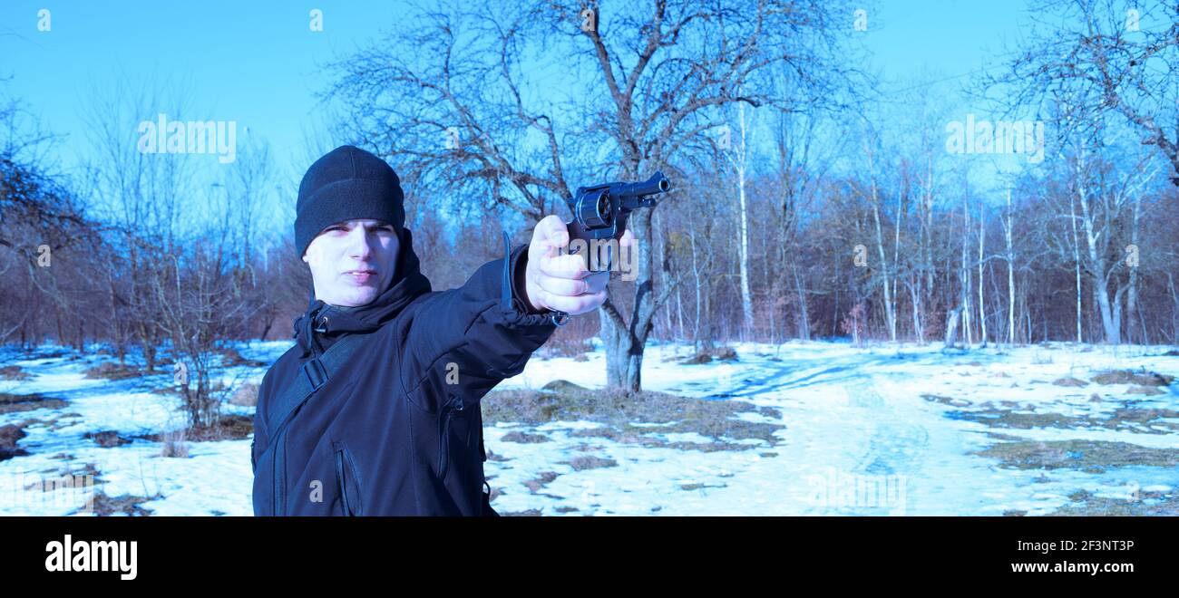 Young man in black clothes shoots with a pistol on nature in winter near the forest Stock Photo
