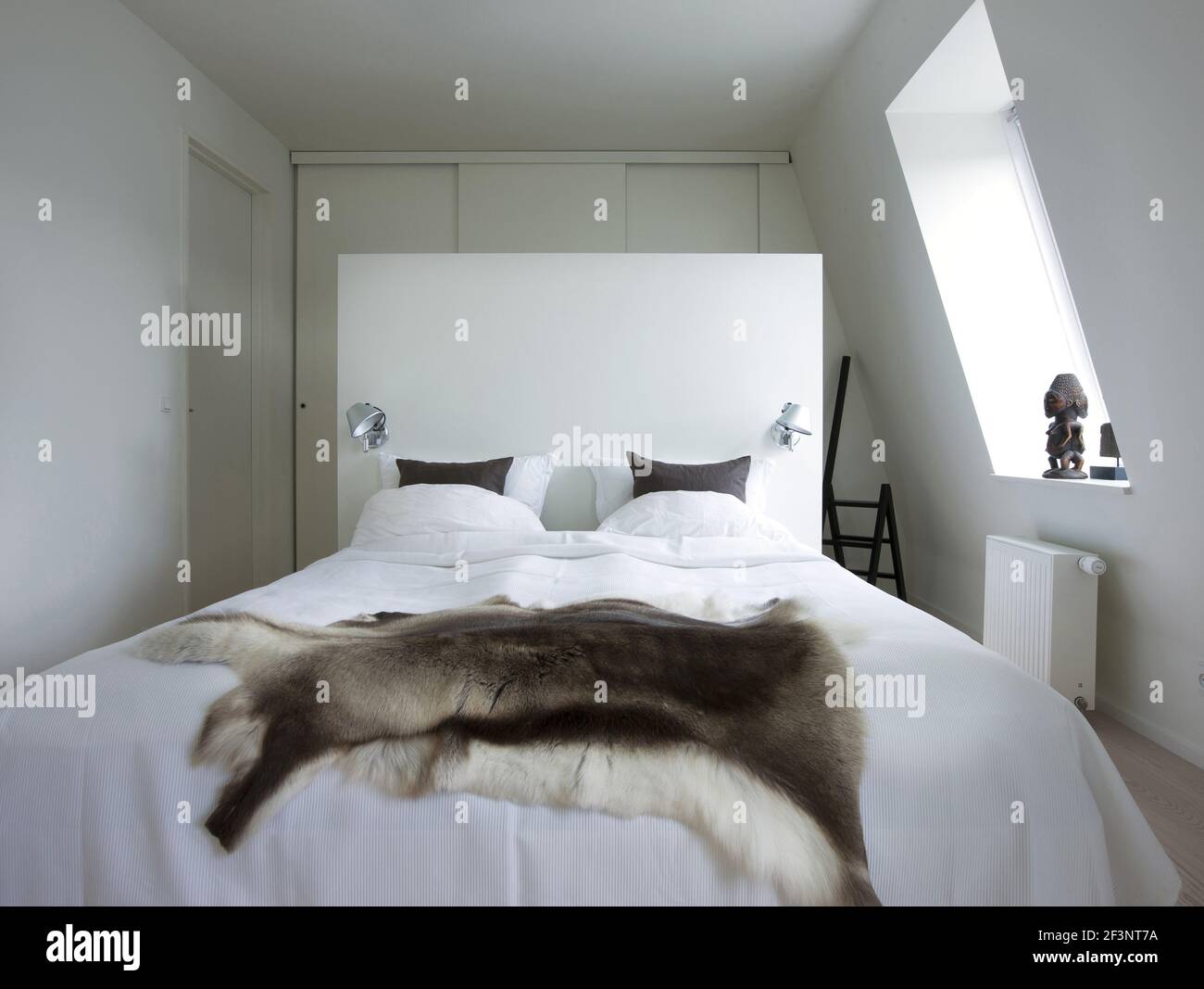 No nonsense, Modern apartment in Copenhagen. White walls and a wooden floor. Art pieces and minimalist style. A bedroom. Animal fur throw. Stock Photo