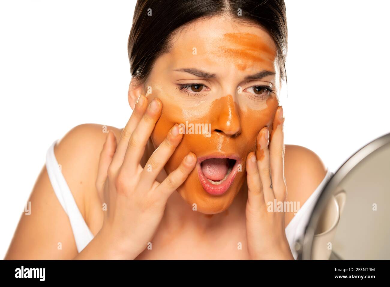 Young shocked woman with wrong makeup base on her face on white background Stock Photo