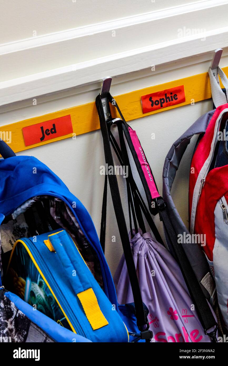 Children's school bags hanging from pegs in a primary school cloakroom. Stock Photo