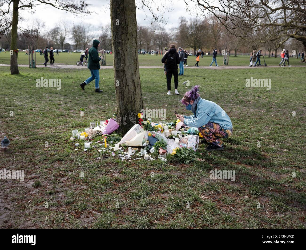 A mourner places flowers and light candles for Sarah Everard at the base of a tree, near the bandstand in Clapham Common, March 14, 2021 Stock Photo
