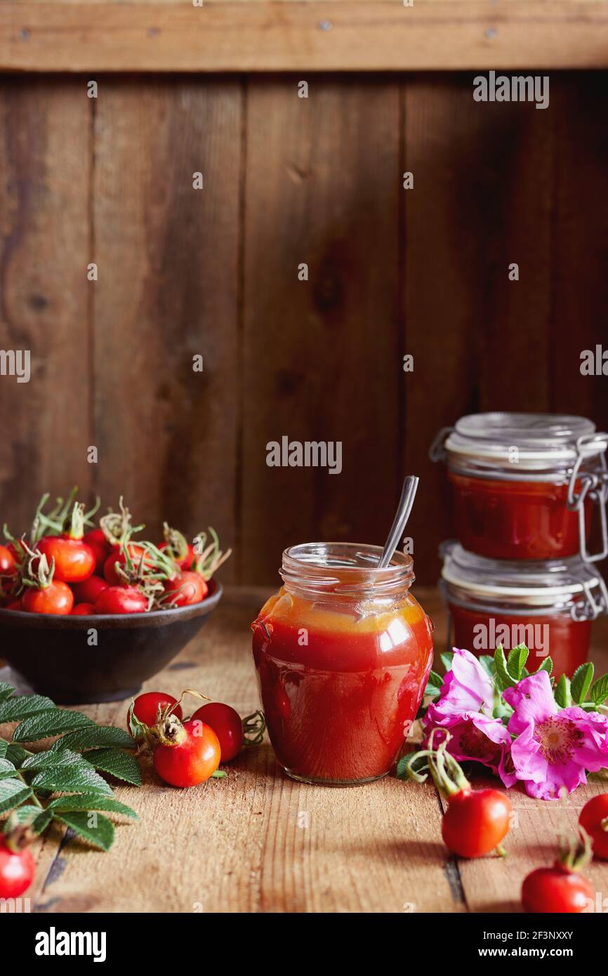 A jar of rose hip jelly and fresh rose hips on wooden table. Stock Photo