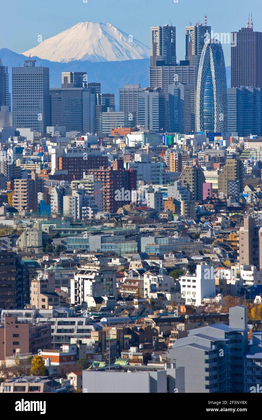 A telephoto view on a clear winter day captures a snow-capped Mt. Fuji rising dramatically beyond the skyscrapers, including Tokyo City Hall, in the S Stock Photo
