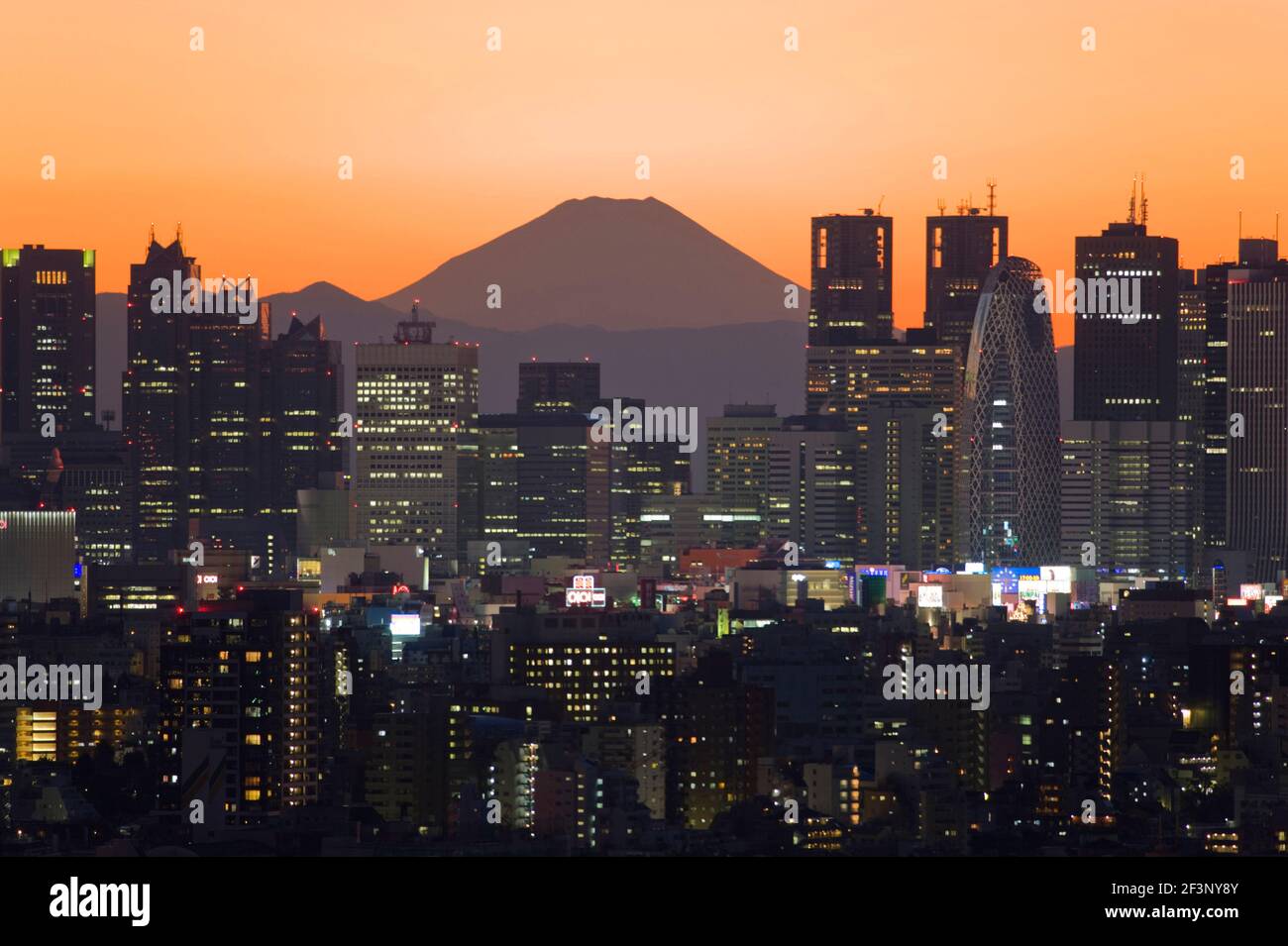 A telephoto view in clear winter twilight captures Mt. Fuji's distinctive peak rising dramatically beyond the skyscrapers (including Tokyo City Hall) Stock Photo