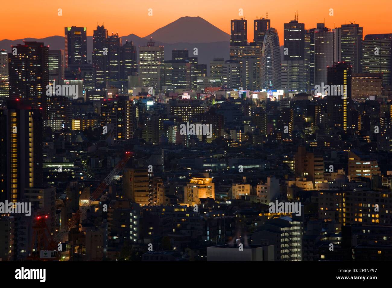 A telephoto view in clear winter twilight captures Mt. Fuji's distinctive peak rising dramatically beyond the skyscrapers (including Tokyo City Hall) Stock Photo