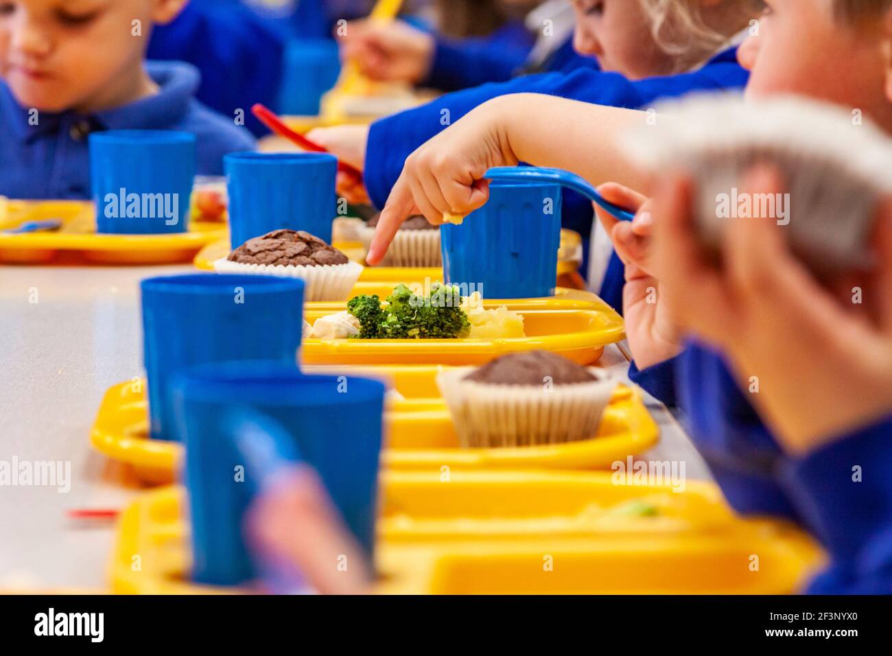 Children at a primary school eating school dinner using plastic plates, cups and cutlery. Stock Photo