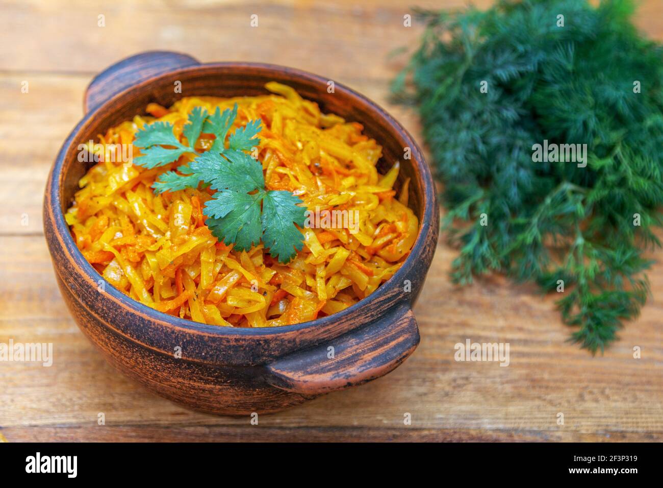 Braised cabbage, stewed with tomato sauce, served in a bowl on wooden table with green onion, parsley and dill Stock Photo