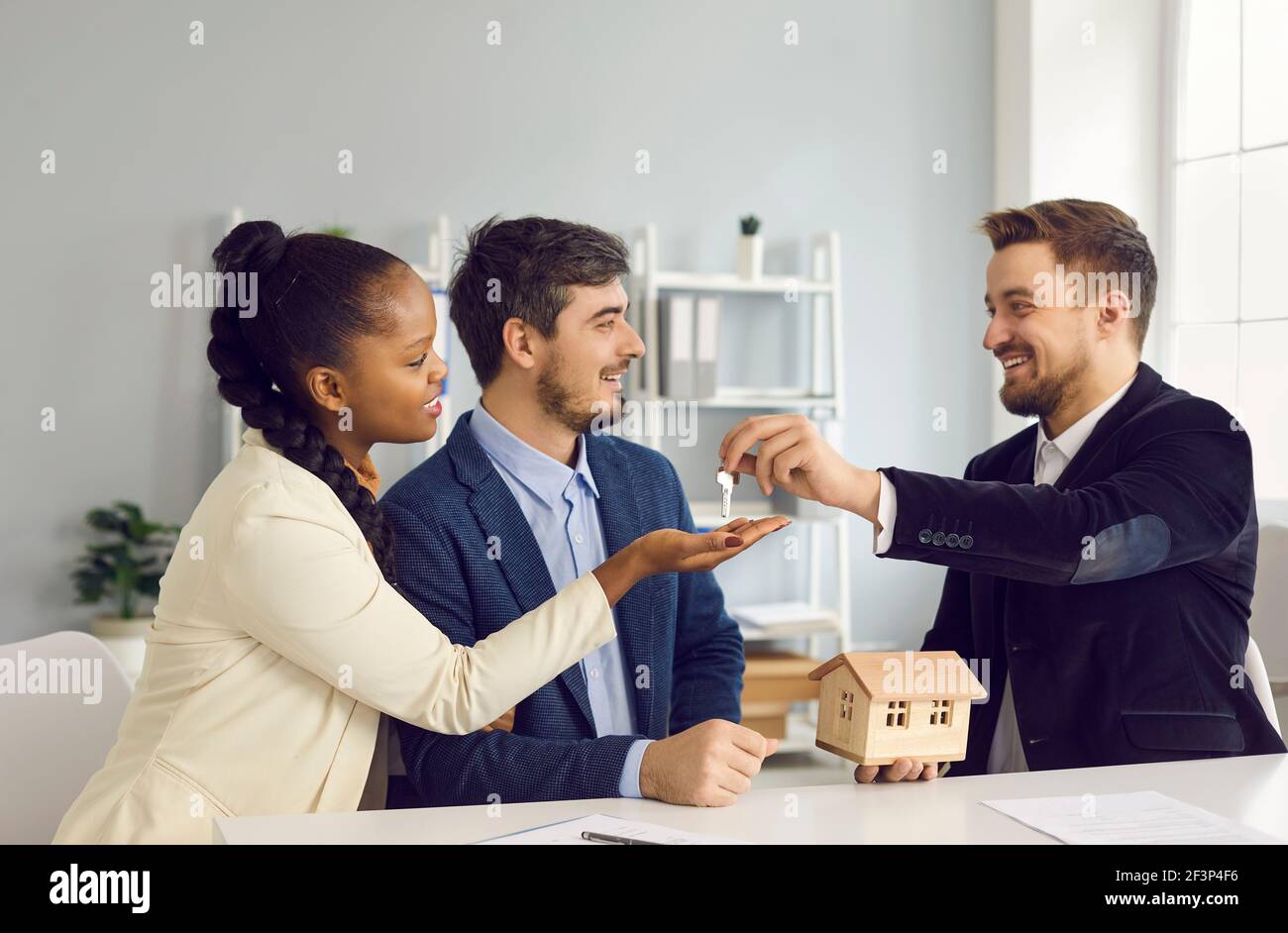 Happy smiling millennial multiethnic couple taking key from realtor agent Stock Photo