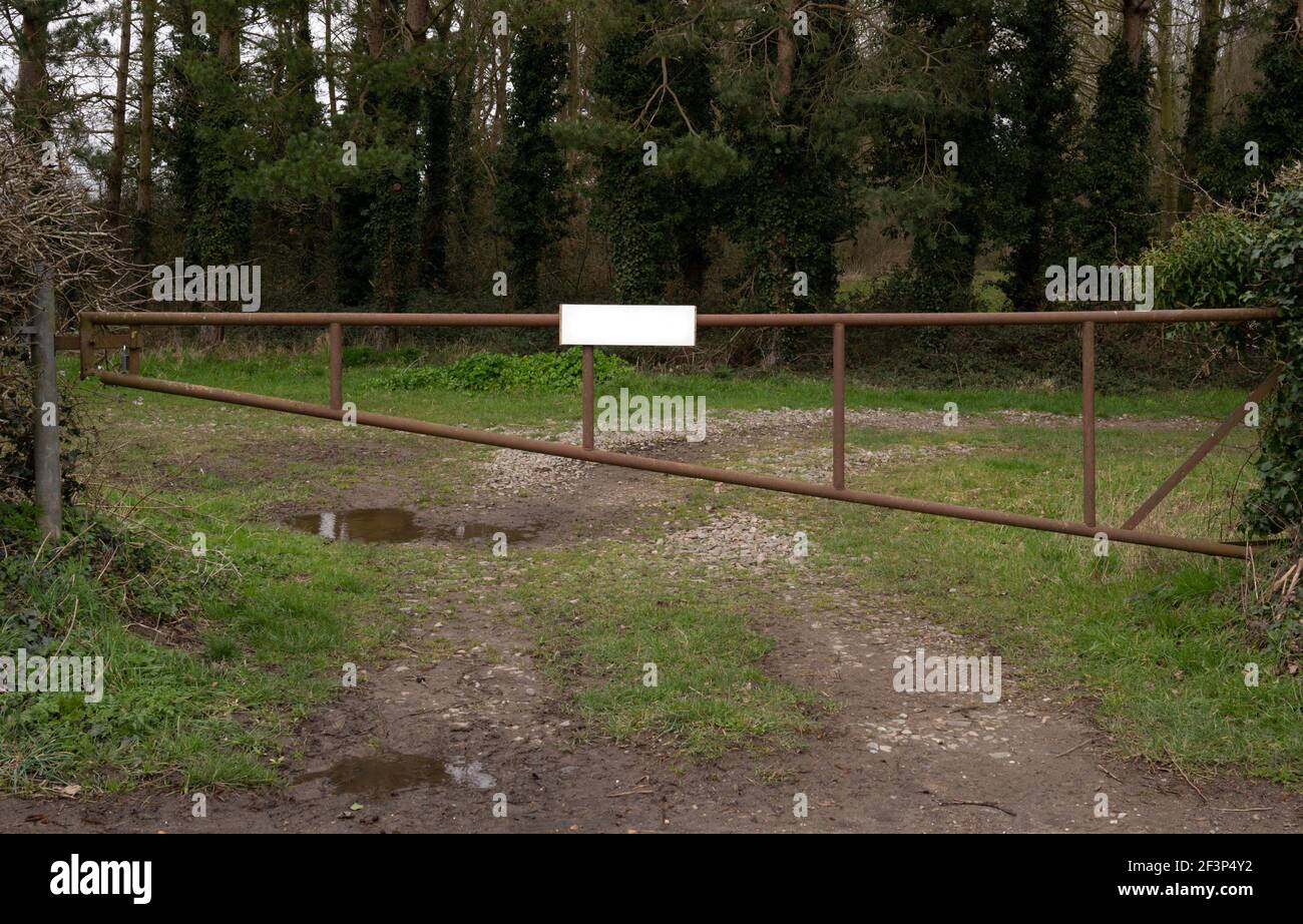 A closed rusty metal gate with a white sign, across a farmers field. Stock Photo