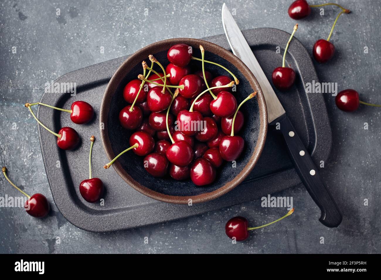 Cherries in a small bowl and scattered around the table. Stock Photo
