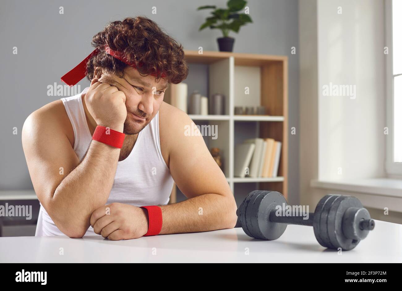 Funny fat man looking at small barbell unsure whether he needs to start training Stock Photo