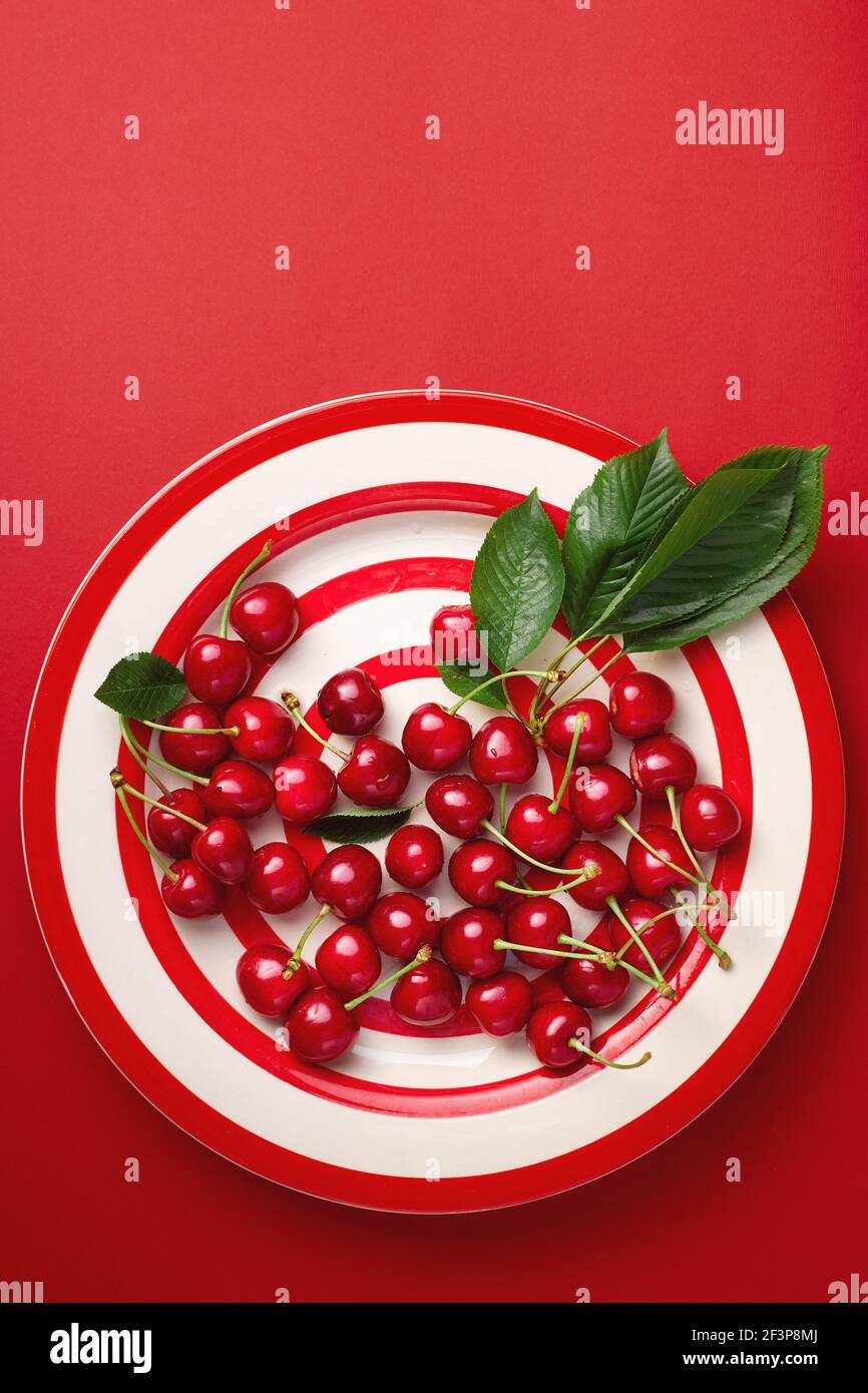 Fresh cherries with leaves on a red striped plate Stock Photo