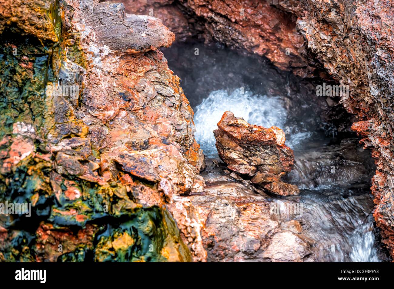 Closeup of steam geyser in Deildartunguhver hot springs in Iceland with red rock colorful cave opening hole and water boiling Stock Photo