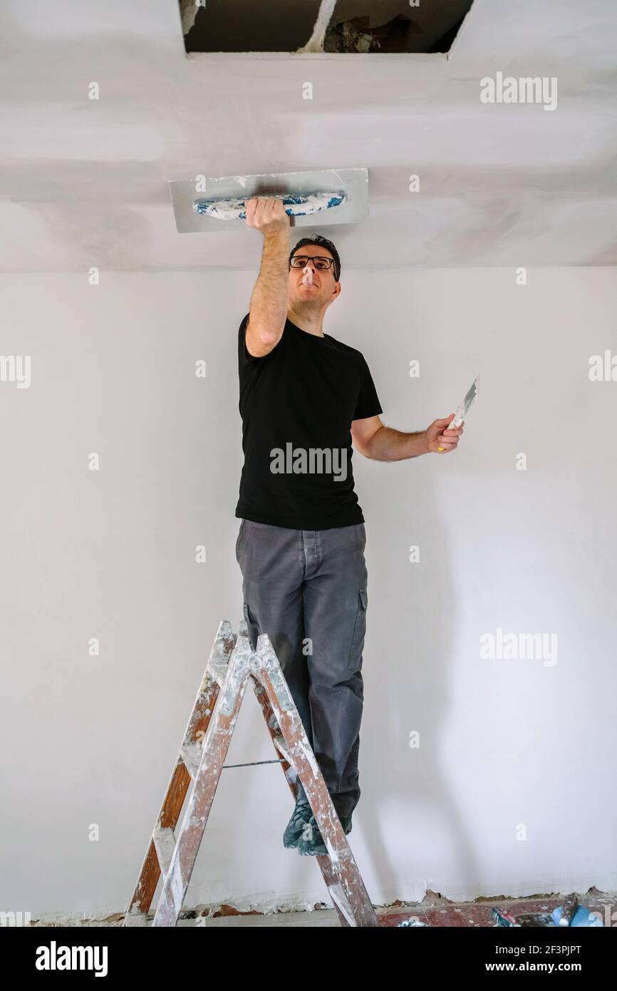 Plasterer smoothing plaster ceiling with the trowel Stock Photo