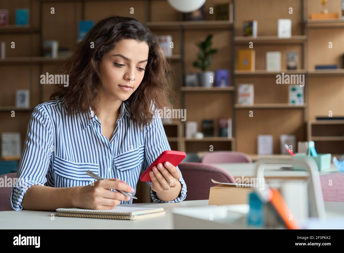 Hispanic latin girl college student holding smartphone studying in university. Stock Photo