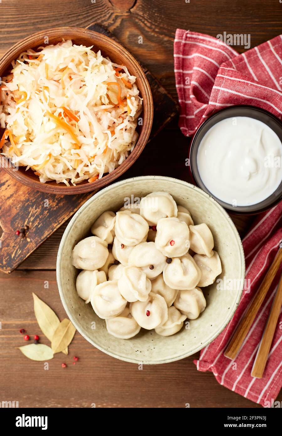 Traditional Russian pelmeni dumplings with sour cream and sauerkraut with sour cream over wooden background. Top view, flat lay. Stock Photo