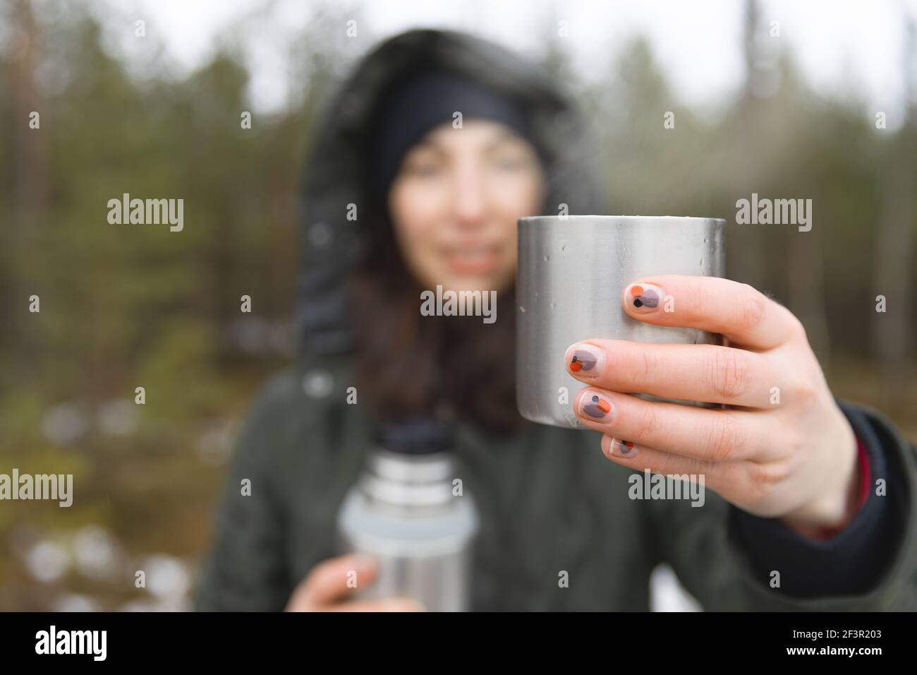 Young women holding a cup of hot beverage with steam during a cold and rainy day. Hiking and healthy living. Stock Photo