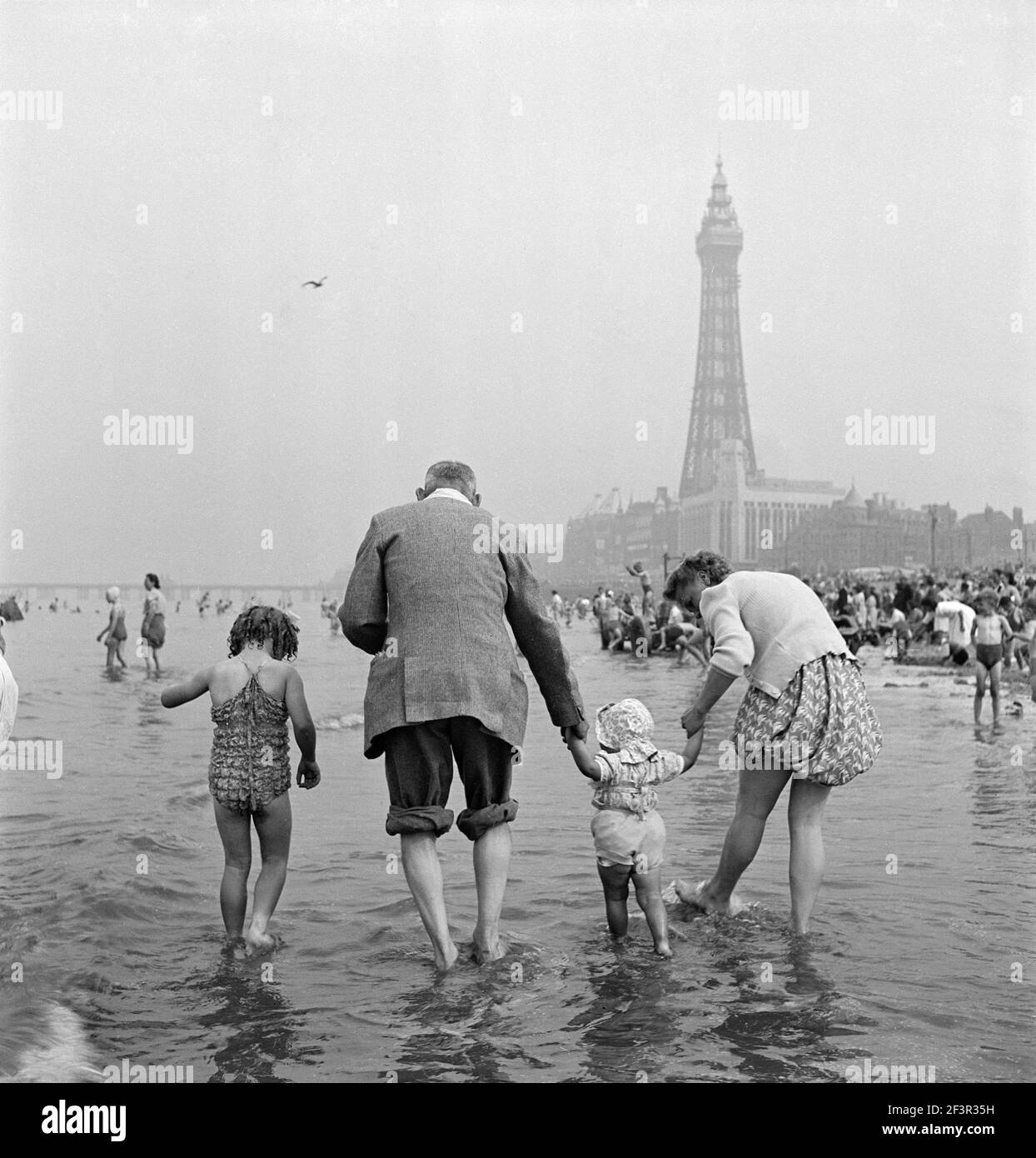 BLACKPOOL, Lancashire. Informal portrait showing rear view of a family with two small daughters paddling in the sea, with Blackpool Tower in the backg Stock Photo