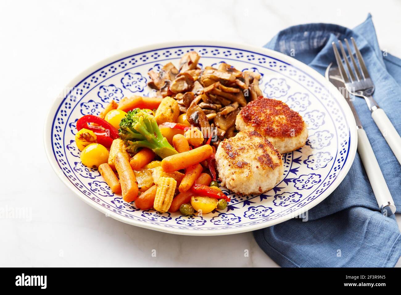 Mixed vegetables of carrots, broccoli, baby corn, bell peppers, roasted champignons and two chicken patties in breadcrumbs Stock Photo