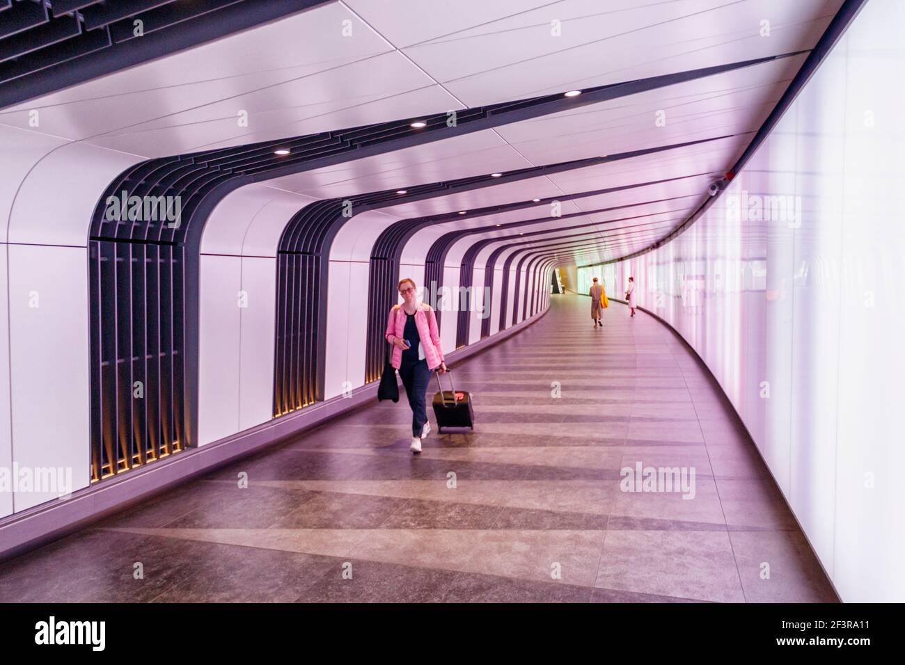 A oman pulling a wheeled suitcase in the underground pedestrian tunnel and lightwall leading from from King's Place to King's Cross-St Pancras Station Stock Photo