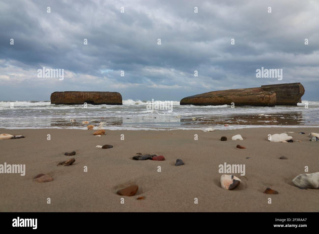 A natural view of small stones on a sandy beach under a cloudy sky ...