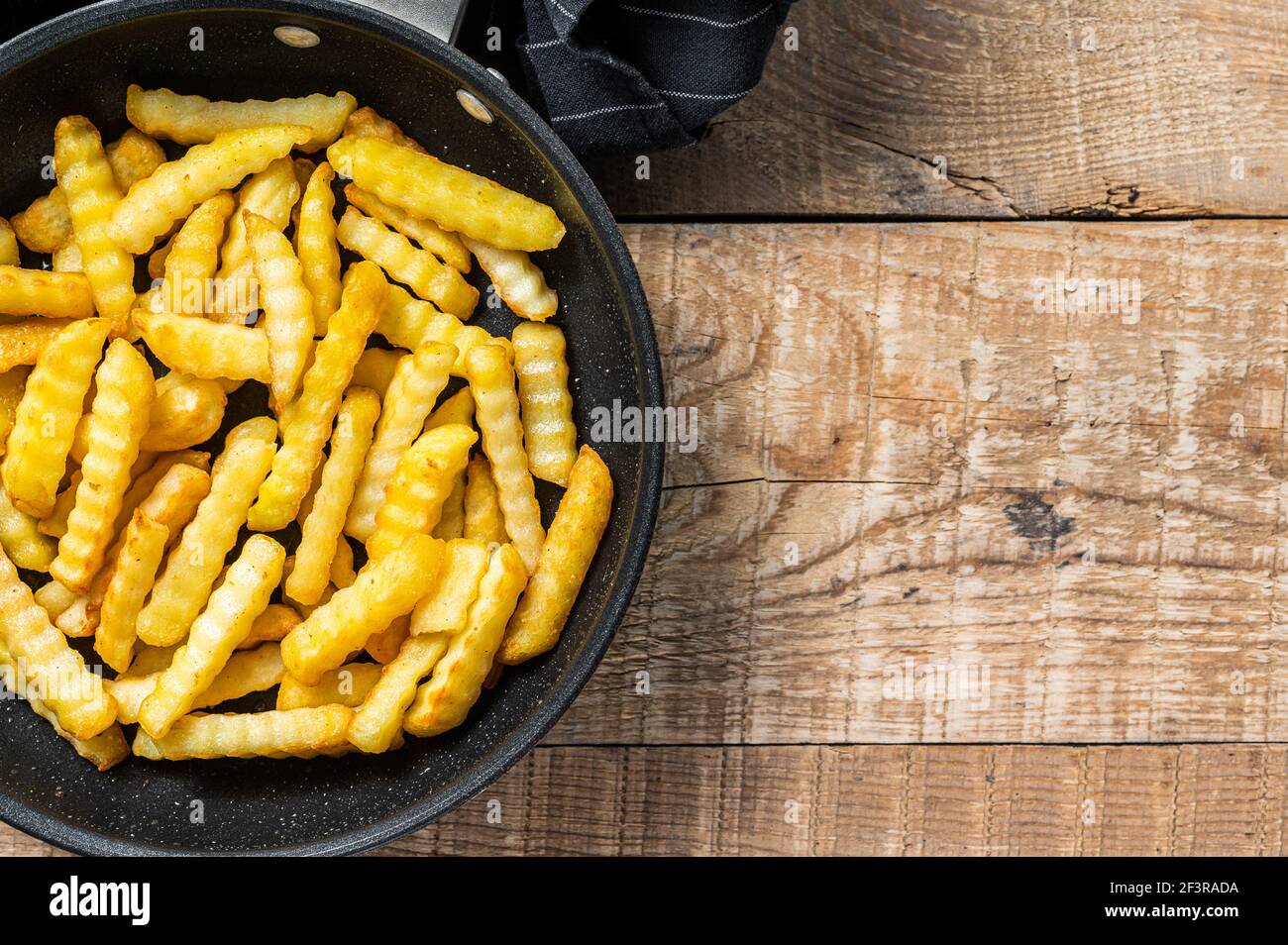 Deep fried Crinkle French fries potatoes sticks in a pan. Wooden