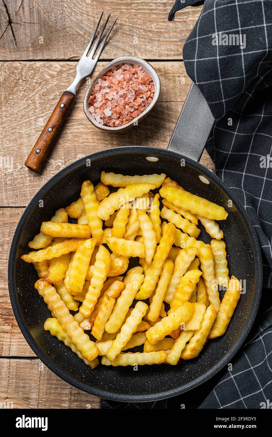 Deep fried Crinkle French fries potatoes sticks in a pan. Wooden