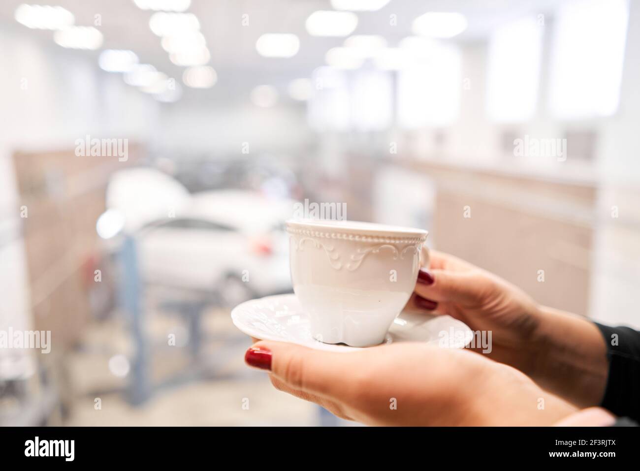 Woman drinking coffee while waiting car in the auto service station. Looking at her car sitting in waiting room of the auto service center Stock Photo