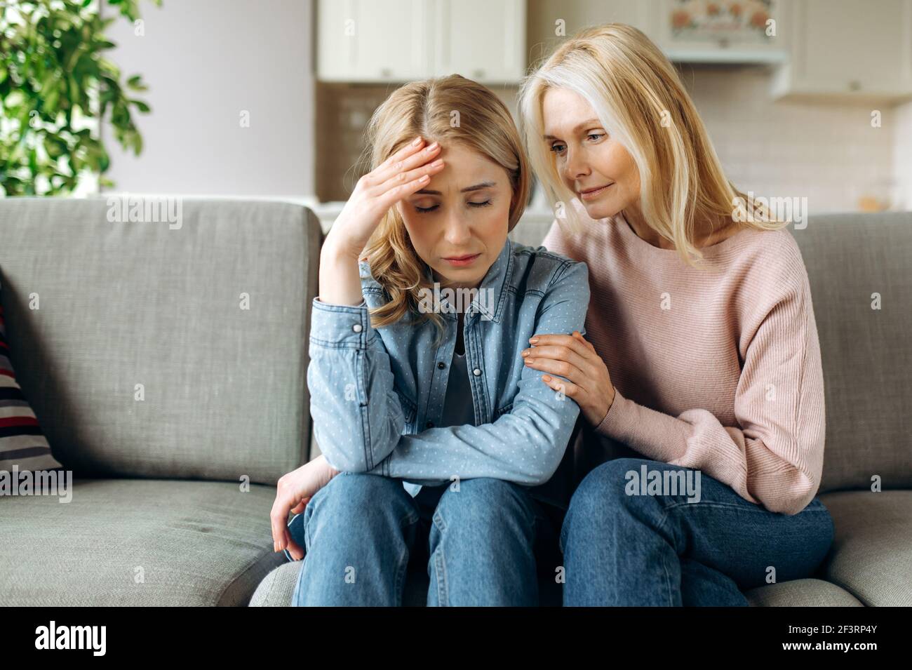 Mother and daughter together at living room. Loving mature mom sits on the couch and hugs her young adult daughter, stroking her, sympathizes, family relationship and values concept Stock Photo