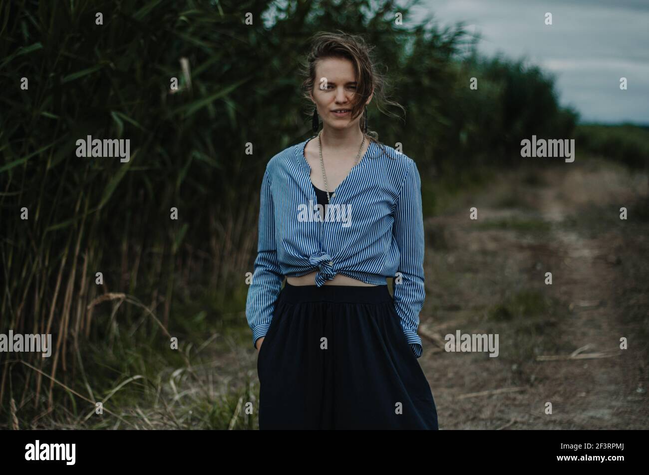 Portrait of a young caucasian woman with neutral expression, near reeds on a path, moody vibe Stock Photo
