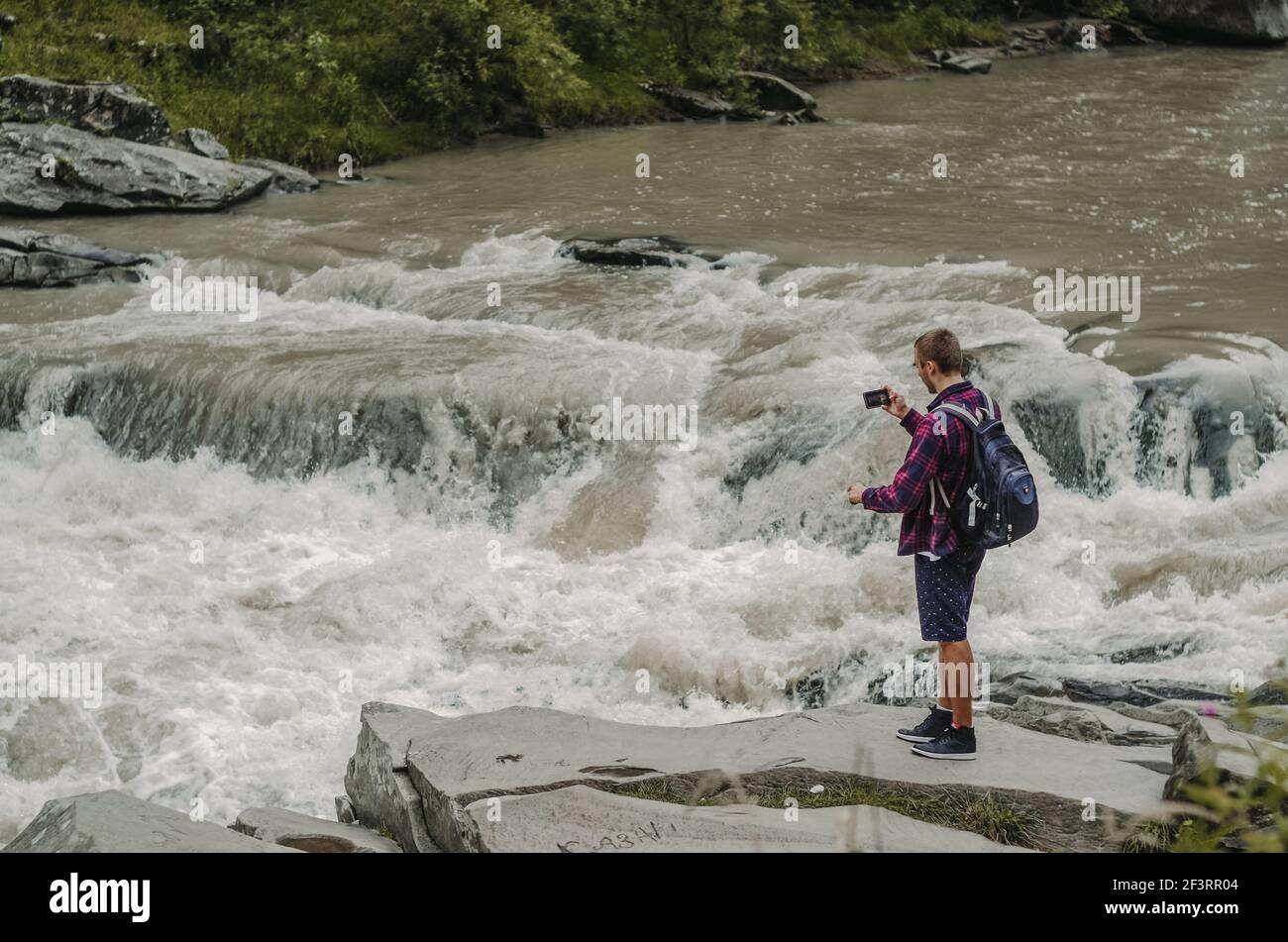 Young man with backpack traveller, taking photos of river Prut in Yaremcha, Ukraine Stock Photo