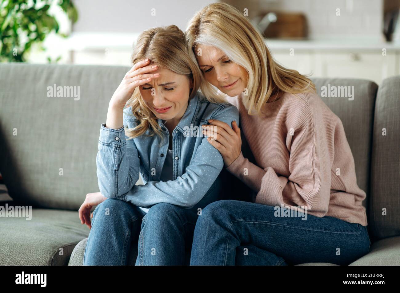Mother and daughter together at living room. Loving mature mom sits on the couch, hugs her young adult crying daughter, stroking her, sympathizes, family relationship and values concept Stock Photo