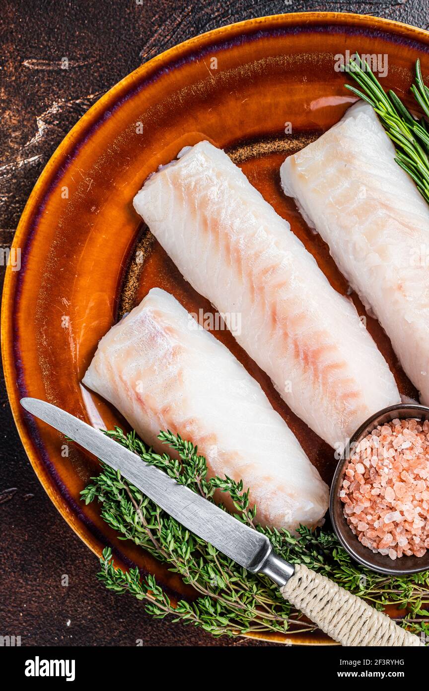 Raw Haddock loin fillet fish on rustic plate with thyme and salt. Dark