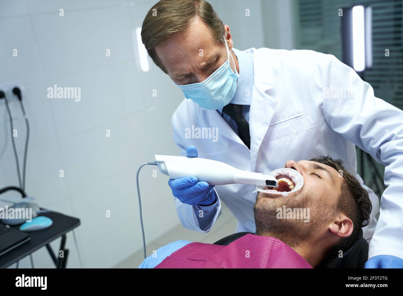 Serious doctor curing teeth of a male patient Stock Photo - Alamy